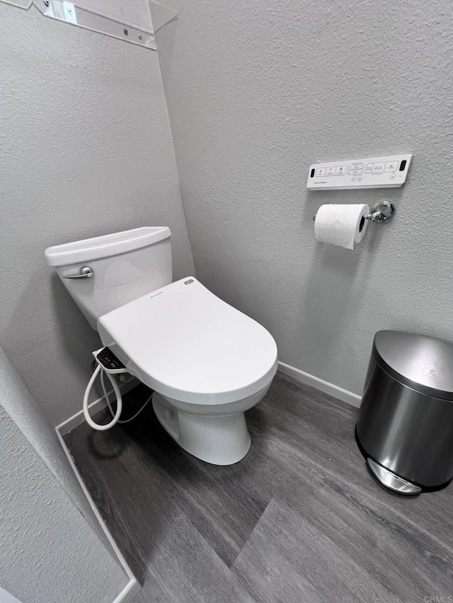 bathroom featuring toilet, wood finished floors, baseboards, and a textured wall