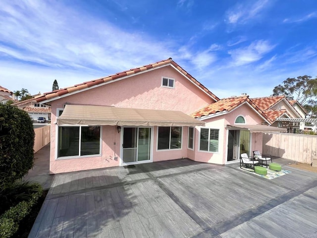 rear view of property with stucco siding, a deck, and fence