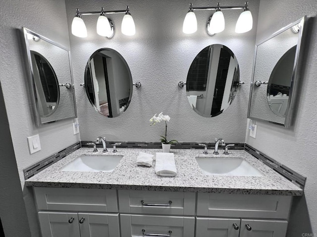 full bathroom featuring double vanity, a textured wall, and a sink