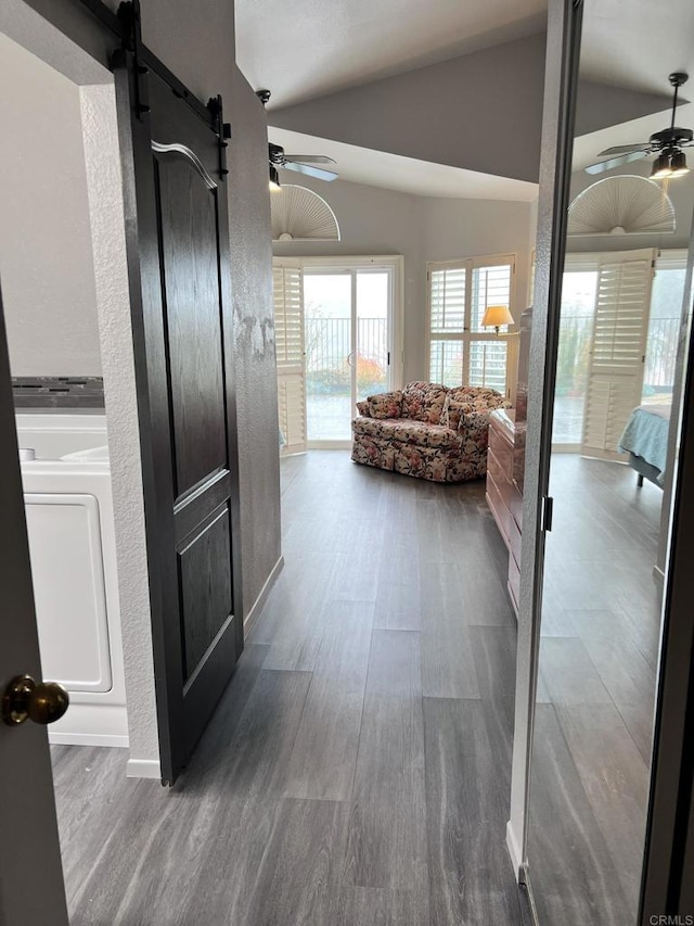 hallway with washer / dryer, wood finished floors, a barn door, and vaulted ceiling