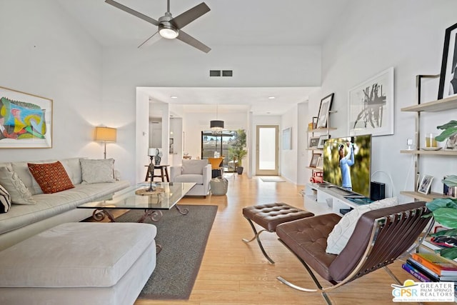 living room featuring ceiling fan, light hardwood / wood-style floors, and a towering ceiling