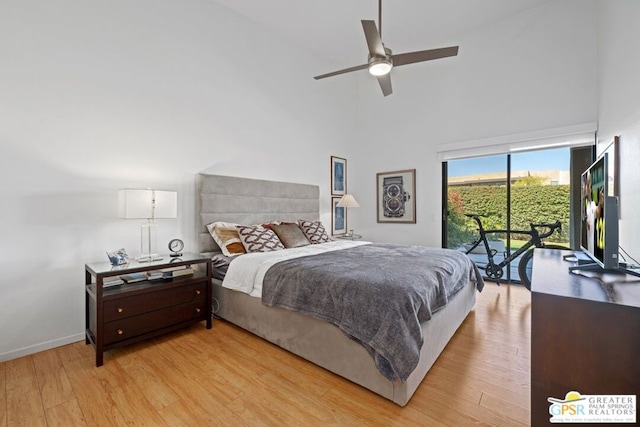 bedroom featuring access to outside, light hardwood / wood-style floors, ceiling fan, and a high ceiling