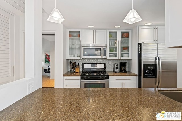 kitchen with white cabinetry, dark stone countertops, appliances with stainless steel finishes, pendant lighting, and decorative backsplash