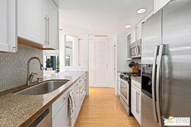 kitchen with appliances with stainless steel finishes, white cabinetry, sink, dark stone countertops, and light hardwood / wood-style flooring