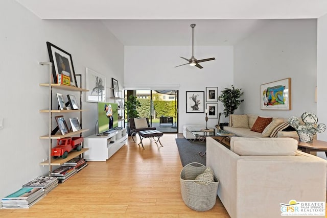 living room featuring a high ceiling, ceiling fan, and light wood-type flooring