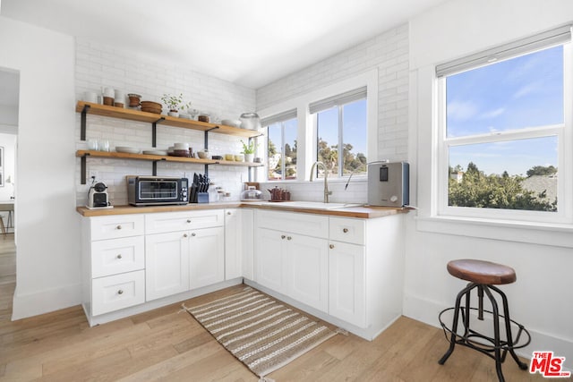 kitchen with sink, light hardwood / wood-style flooring, white cabinetry, tasteful backsplash, and wood counters