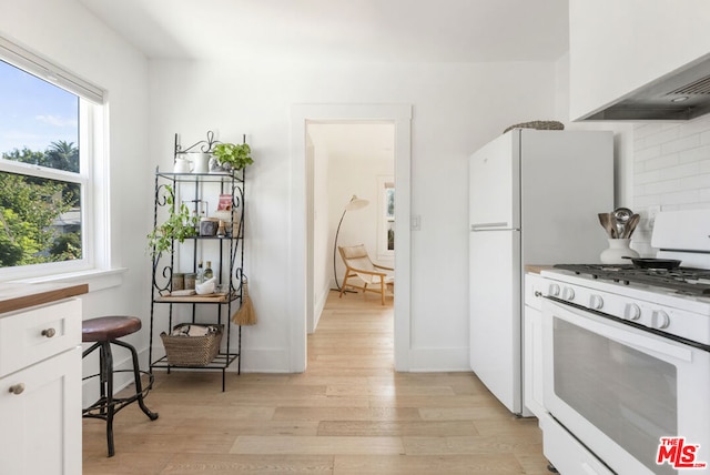 kitchen with white range with gas stovetop, white cabinetry, tasteful backsplash, custom range hood, and light hardwood / wood-style floors