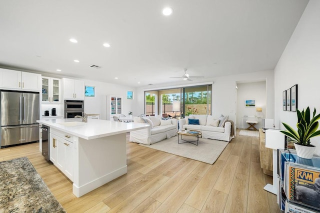 kitchen featuring light hardwood / wood-style floors, an island with sink, white cabinets, and appliances with stainless steel finishes