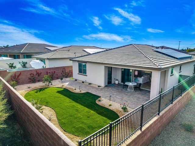 rear view of house with a yard, a patio, and solar panels