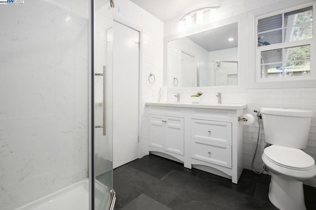 bathroom with a shower with door, vanity, tile walls, and toilet