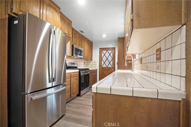 kitchen with sink, backsplash, stainless steel appliances, tile counters, and light wood-type flooring