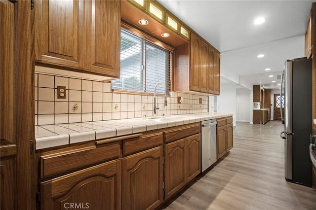 kitchen featuring sink, tile counters, stainless steel appliances, and light hardwood / wood-style floors