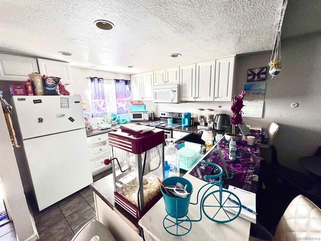 kitchen with a textured ceiling, white cabinets, white appliances, and dark tile patterned flooring