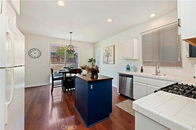 kitchen featuring decorative light fixtures, stainless steel dishwasher, a kitchen island, white fridge, and white cabinets