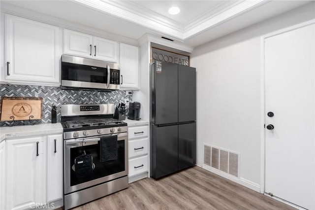 kitchen featuring white cabinetry, appliances with stainless steel finishes, light wood-type flooring, and a tray ceiling