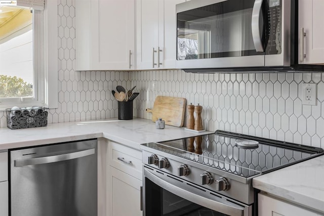 kitchen with white cabinetry, appliances with stainless steel finishes, light stone countertops, and decorative backsplash