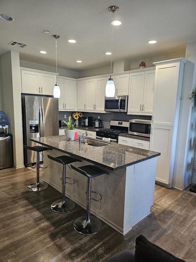 kitchen with a breakfast bar area, hanging light fixtures, stainless steel appliances, white cabinets, and a center island with sink