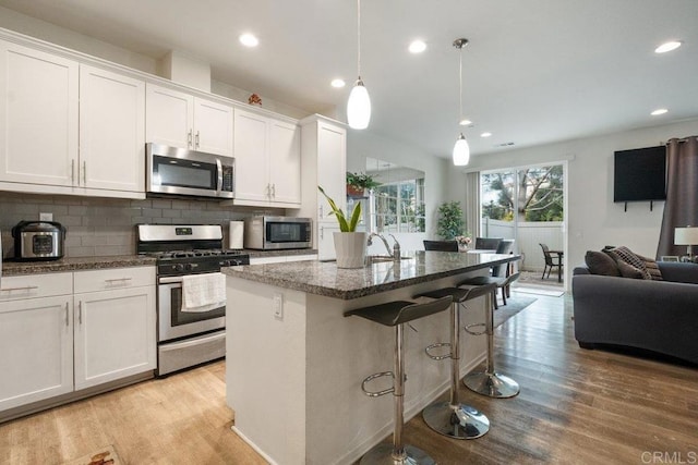 kitchen with stainless steel appliances, white cabinetry, hanging light fixtures, and a kitchen island with sink