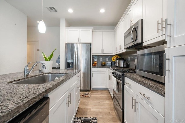 kitchen with stainless steel appliances, sink, dark stone countertops, and white cabinets