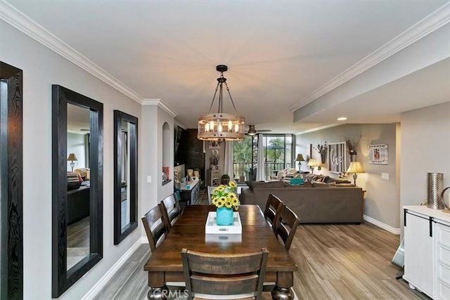 dining space with light wood-style floors, baseboards, ornamental molding, and an inviting chandelier