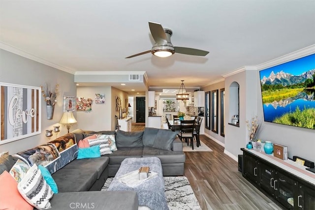 living room featuring wood finished floors, visible vents, baseboards, a ceiling fan, and ornamental molding