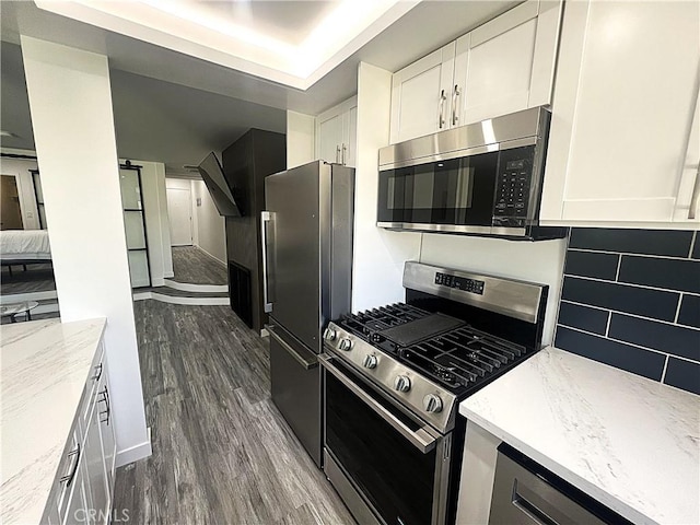 kitchen featuring appliances with stainless steel finishes, white cabinets, decorative backsplash, light stone countertops, and dark wood-type flooring