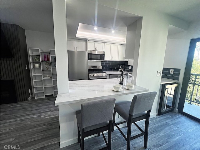 kitchen featuring dark wood-type flooring, a kitchen bar, white cabinetry, stainless steel appliances, and decorative backsplash