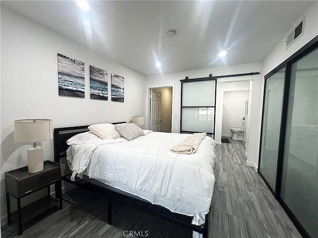 bedroom featuring ensuite bathroom, a barn door, dark hardwood / wood-style floors, and a closet