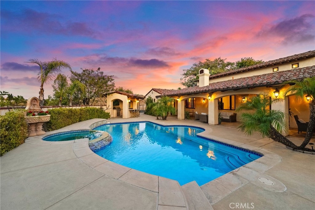 pool at dusk with an outdoor fireplace and a patio