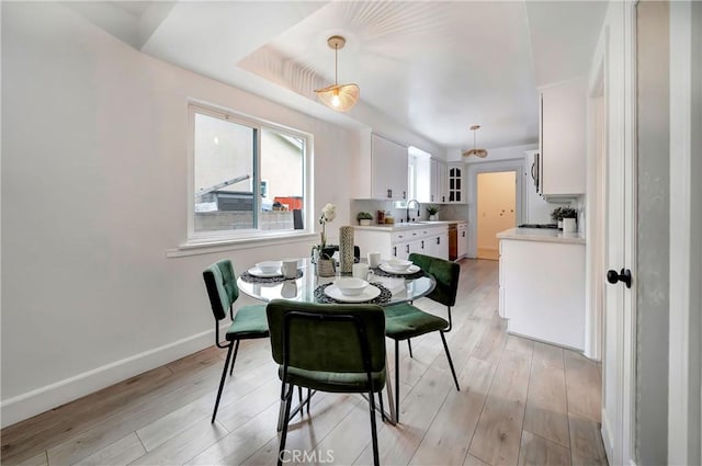 dining area featuring a raised ceiling, sink, and light hardwood / wood-style flooring