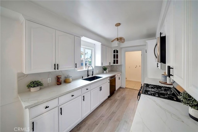 kitchen featuring dishwashing machine, sink, white cabinetry, backsplash, and light stone counters