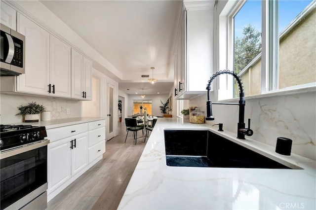 kitchen featuring sink, tasteful backsplash, light stone countertops, gas range oven, and white cabinets