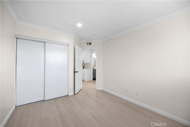 unfurnished bedroom featuring light wood-style flooring, a closet, baseboards, and crown molding