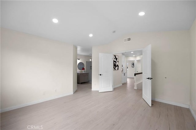 unfurnished room with baseboards, visible vents, vaulted ceiling, light wood-type flooring, and recessed lighting