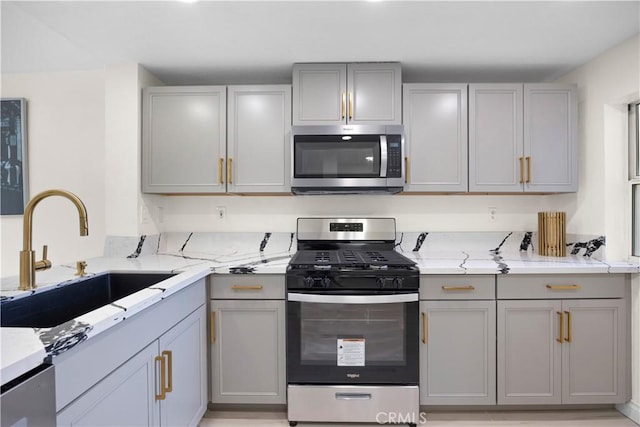 kitchen featuring appliances with stainless steel finishes, gray cabinets, a sink, and light stone counters