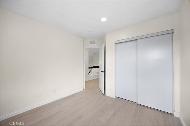 unfurnished bedroom featuring light wood-type flooring, baseboards, visible vents, and a closet