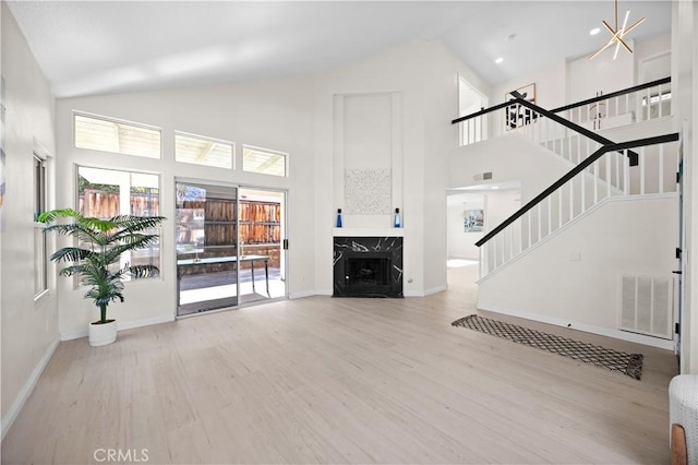 unfurnished living room with visible vents, stairway, a premium fireplace, high vaulted ceiling, and light wood-type flooring