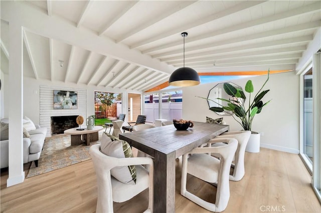 dining area with lofted ceiling with beams, light wood-type flooring, and a fireplace