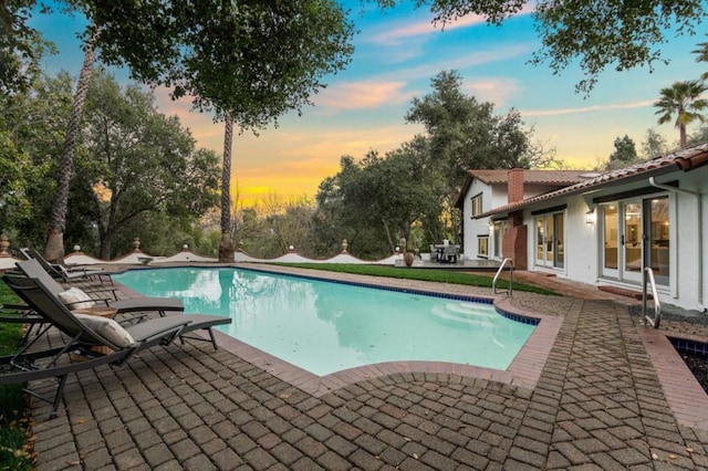 pool at dusk featuring french doors and a patio area