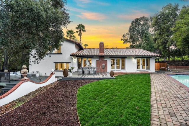 back house at dusk featuring a patio, a yard, and french doors