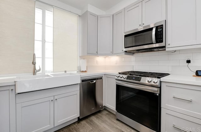 kitchen with sink, stainless steel appliances, light hardwood / wood-style floors, white cabinets, and decorative backsplash