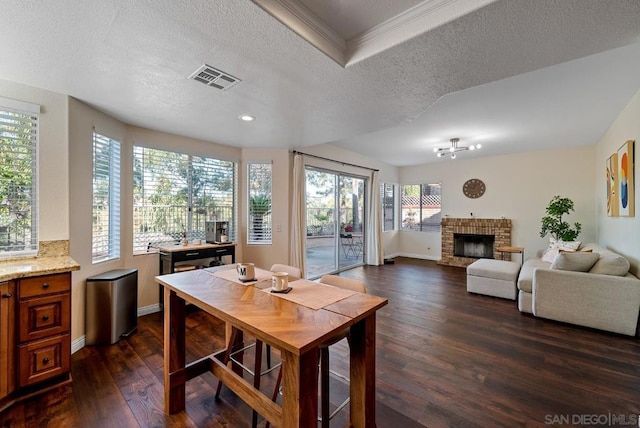 dining area with crown molding, dark hardwood / wood-style flooring, a brick fireplace, and a textured ceiling