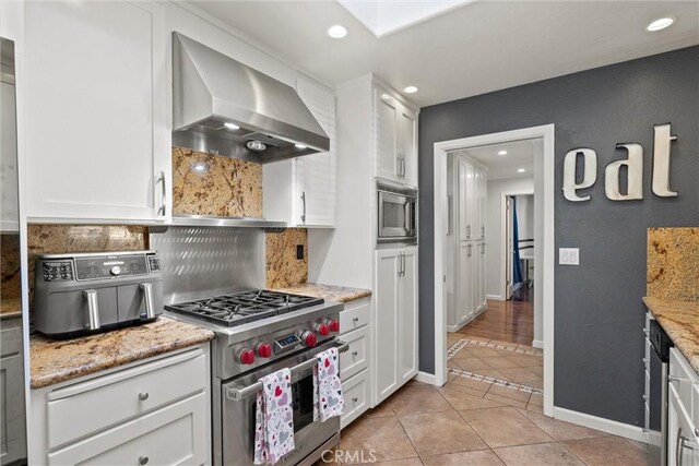 kitchen featuring white cabinetry, appliances with stainless steel finishes, extractor fan, and light stone counters