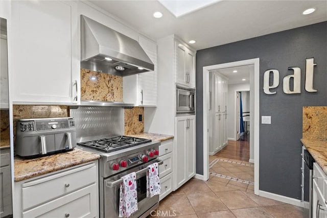 kitchen with light tile patterned floors, decorative backsplash, white cabinets, appliances with stainless steel finishes, and wall chimney exhaust hood