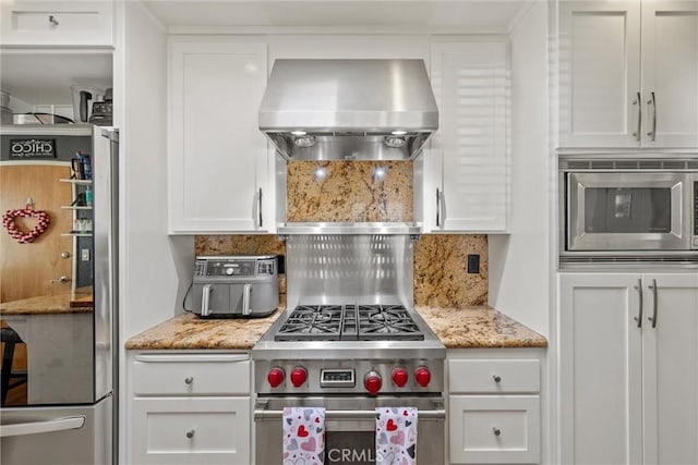 kitchen featuring decorative backsplash, white cabinetry, stainless steel appliances, and wall chimney range hood