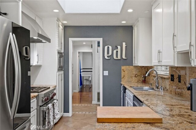 kitchen with appliances with stainless steel finishes, sink, white cabinets, light stone countertops, and wall chimney range hood