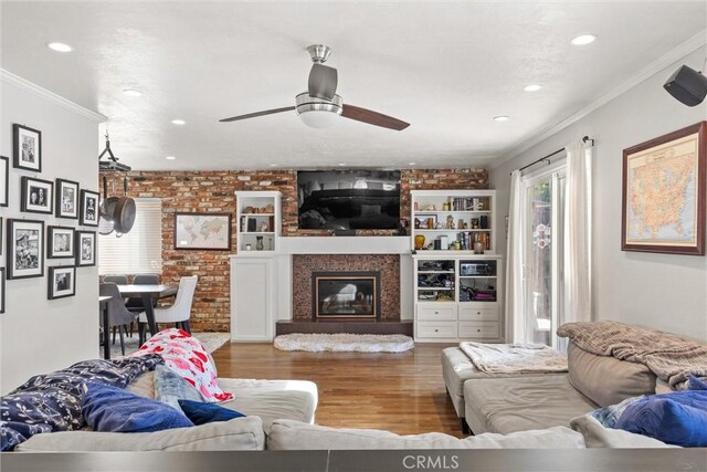 living room featuring crown molding, a large fireplace, ceiling fan, brick wall, and hardwood / wood-style floors