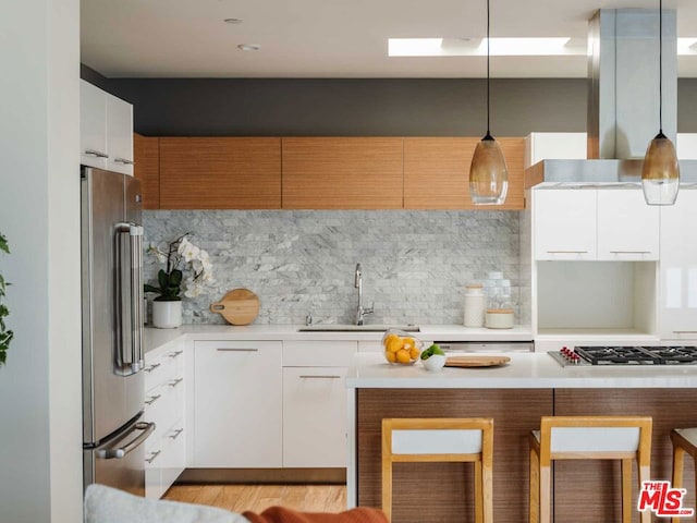 kitchen with wall chimney range hood, decorative light fixtures, white cabinets, and appliances with stainless steel finishes