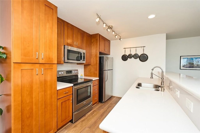 kitchen with sink, backsplash, stainless steel appliances, track lighting, and light wood-type flooring