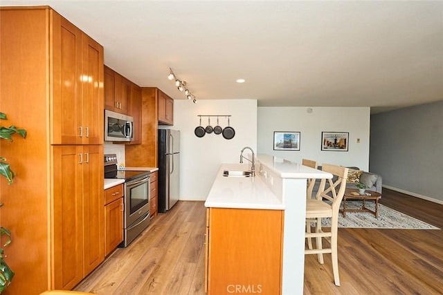 kitchen featuring sink, a breakfast bar area, a center island with sink, appliances with stainless steel finishes, and light hardwood / wood-style floors